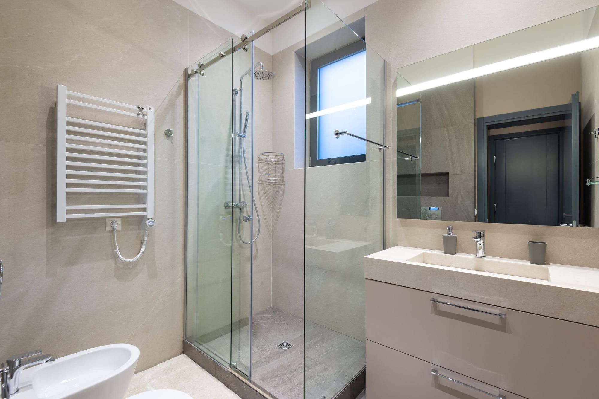 Bagno in toni beige con box doccia in vetro, scaldasalviette e mobile lavabo sospeso
