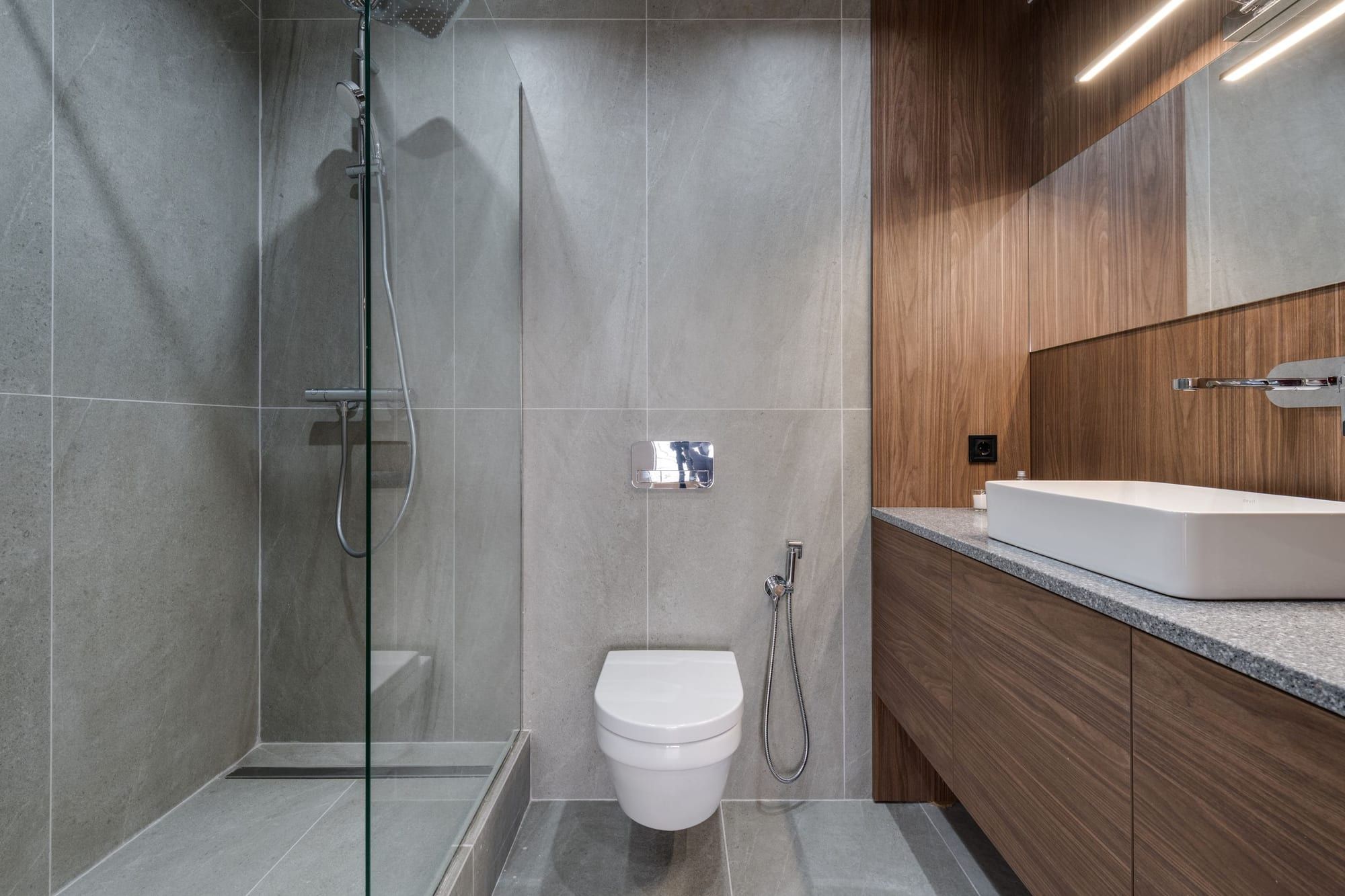 Bagno moderno con doccia a filo pavimento, rivestimenti in pietra grigia e mobile lavabo in noce
