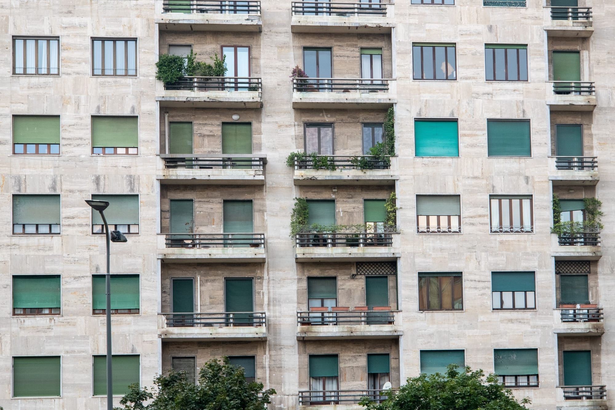 Facciata di un palazzo residenziale milanese in travertino con balconi e persiane verdi