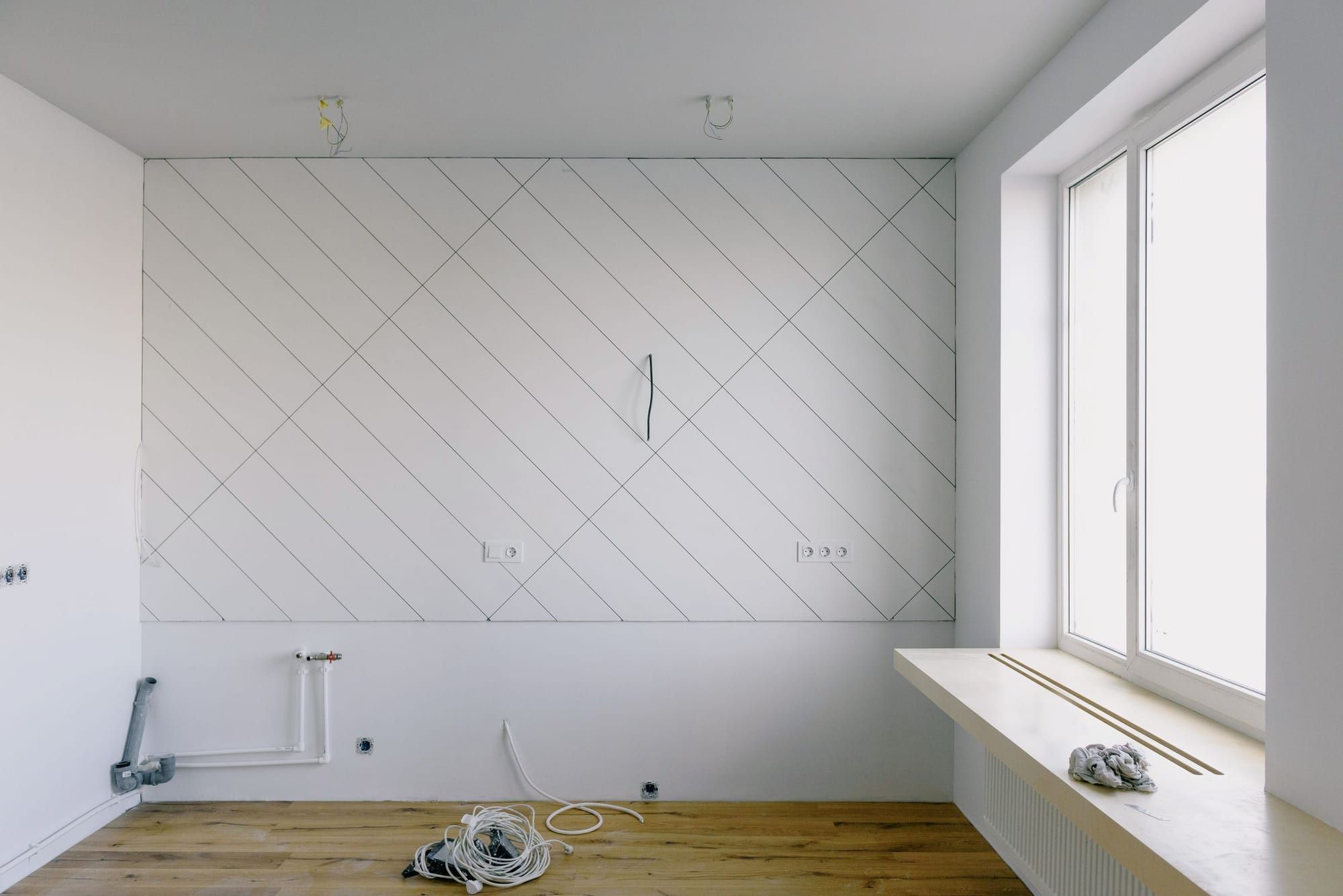Stanza in ristrutturazione con tubazioni idrauliche e scarico predisposti a vista, parquet in rovere e ampia finestra