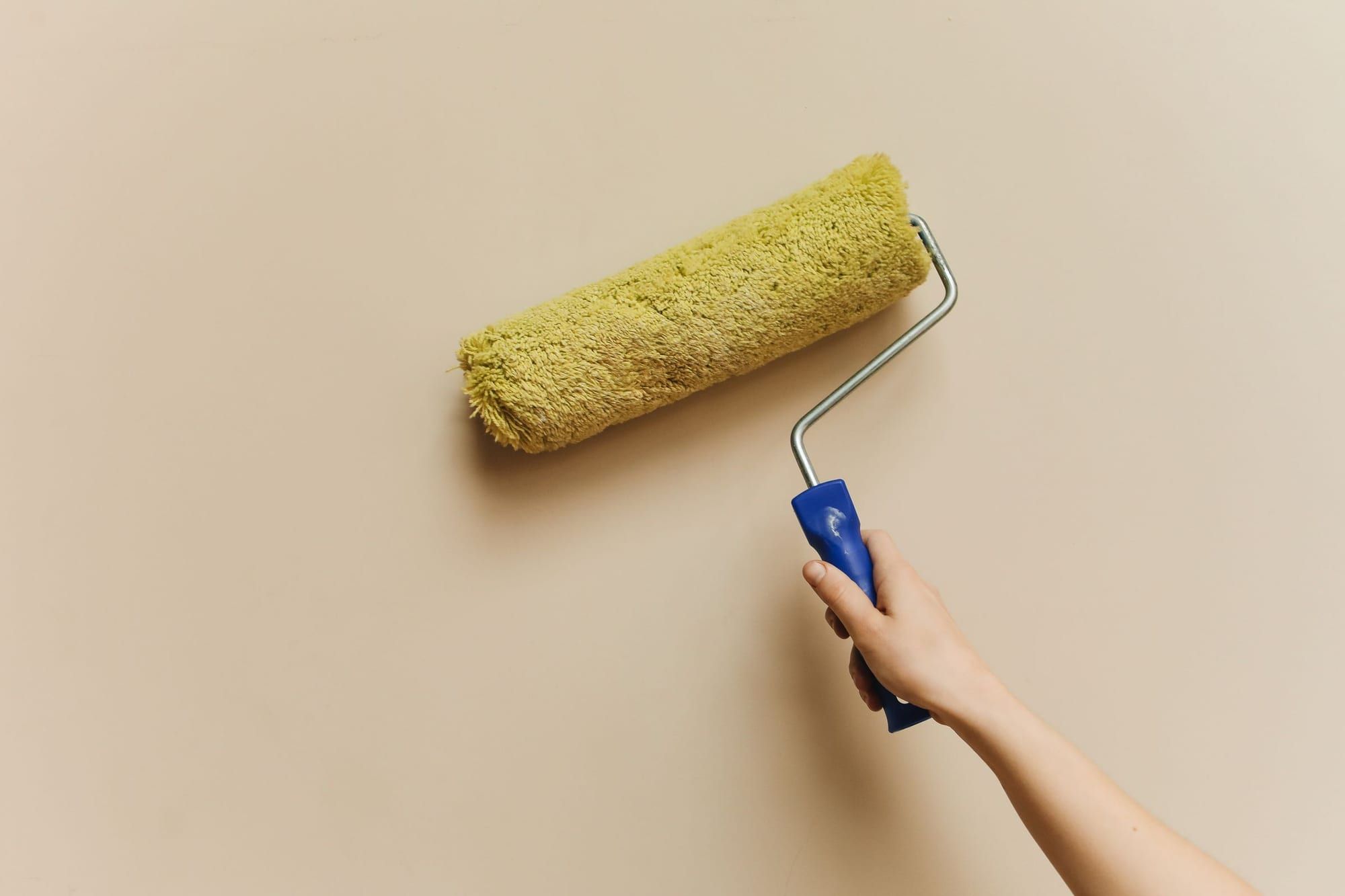 Mano che passa un rullo da pittura su una parete color beige